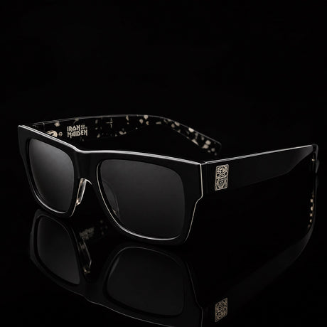 Iron Maiden 50 Years Sunglasses - front three-quarter view, matte black frame, smoke lens, Eddie hinge plaque and Iron Maiden temple logo